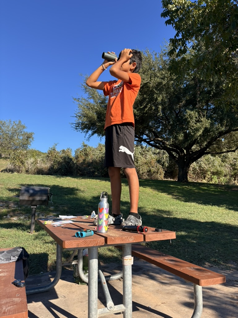 Kid scanning the sky with binoculars from a picnic table