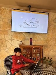 A camper at a laptop with his drawing on the big screen
