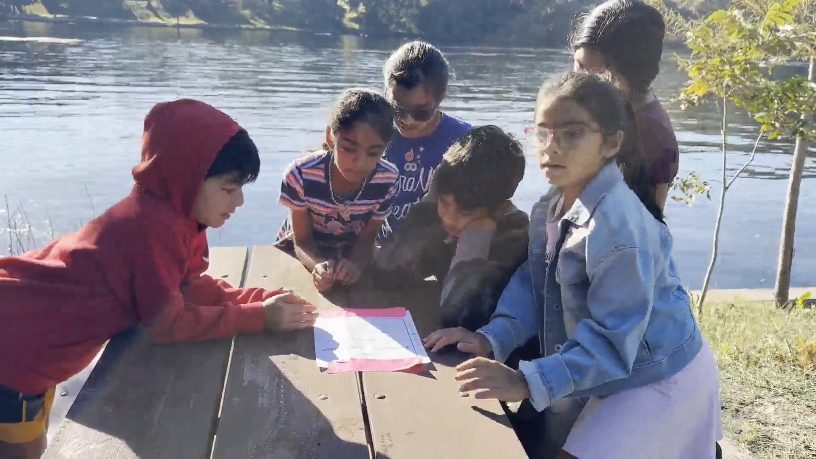 All five campers around a clue sheet at the picnic table